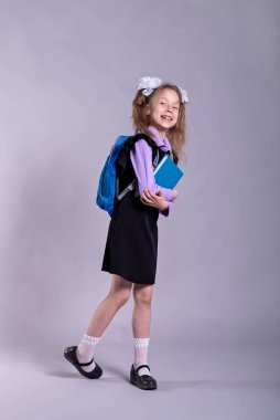 Okul üniformalı, gri arka planda sırt çantası olan bir kız. Okula dönüş konsepti..