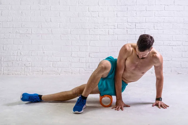 A young man in shorts does exercises on a roller from foam to his legs. Exercise on a foam roller.