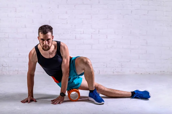 A young man in shorts does exercises on a roller from foam to his legs. Exercise on a foam roller.