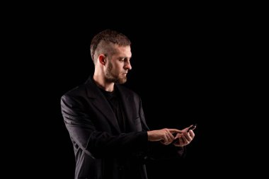 Siyah takım elbiseli bir iş adamının portresi ve siyah arka planda izole edilmiş bir telefon. İşletme tarzı portre.