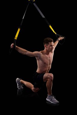 Siyah arka planda izole edilmiş trx fitness kayışlarıyla egzersiz yapan genç kaslı adam. Aktif yaşam tarzı. Sporcu siyah arkaplanda izole edildi.