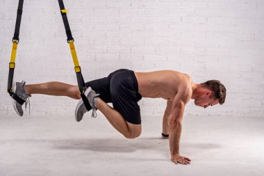 Kaslı genç adam beyaz tuğla bir duvarın yanında kemerleriyle egzersiz yapıyor. Aktif yaşam tarzı, vücut geliştirme.