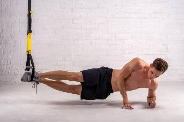 Kaslı bir adam beyaz tuğla bir duvarın yanında kemerlerle egzersiz yapıyor. Vücut geliştirme.