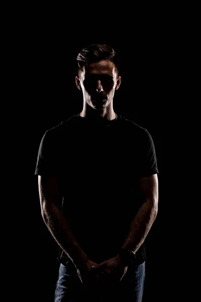 Portrait of a young athletic man in a black T-shirt on a black background. Young beautiful sporty man. Fitness lifestyle.