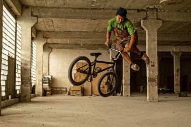 Terk edilmiş bir fabrika binasında atlayış yapan bir BMX bisikletçisi. Aşırı bisiklet sürme. Şehir gezisi.