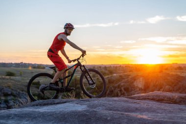 Bisikletçi, gün batımının arka planında, bir dağ bisikleti üzerinde kayalara biniyor, boş alanın bir kopyası. Aktif yaşam tarzı, bisikletçilik. MTB.