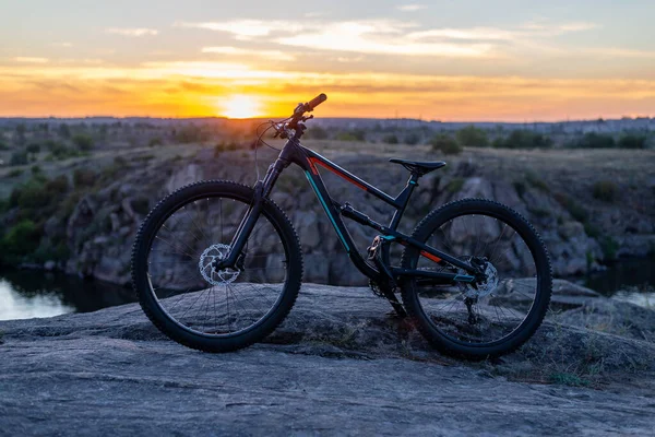 A full suspension mountain bike stands on a rock against the backdrop of a sunset. MTB. Cycling concept.