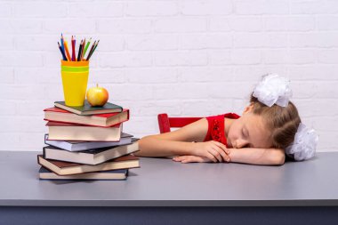 Yorgun bir liseli kız masasında uyuyakaldı. Çocuk bir masada oturuyor..