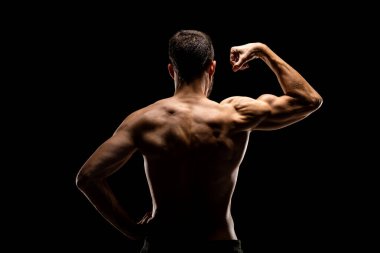 Kaslı güçlü bir adam siyah arka planda izole edilmiş kaslı bir şekilde geriye bakıyor. Vücut geliştirme.