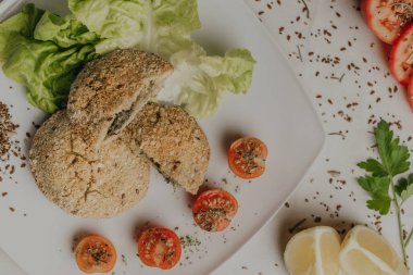 Plato de comida sana sobre fondo de mantel blanco. Dieta de Milanesas de quinoa rellenas de espinaca y queso, acompaadas de lechuga y tomates cherry. Dieta kurtarılabilir.