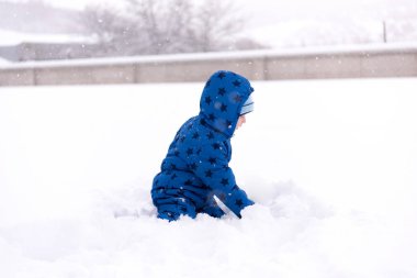 Çocuk, üç yaşında kışlık kıyafetler içinde kar ile oynarken.