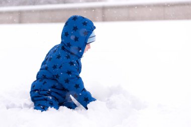 Çocuk, üç yaşında kışlık kıyafetler içinde kar ile oynarken.