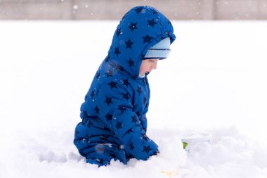 Çocuk, üç yaşında kışlık kıyafetler içinde kar ile oynarken.