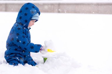 Çocuk, üç yaşında kışlık kıyafetler içinde kar ile oynarken.