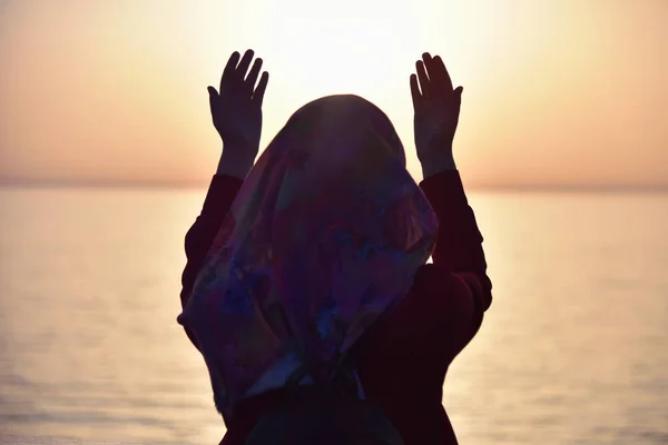 Muslim woman praying in the ship praying at sunset with hands up