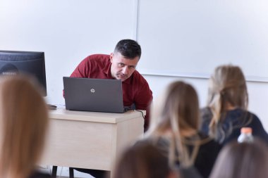 Erkek profesör öğrencilere ders veriyor ve onlarla iletişim kuruyor.