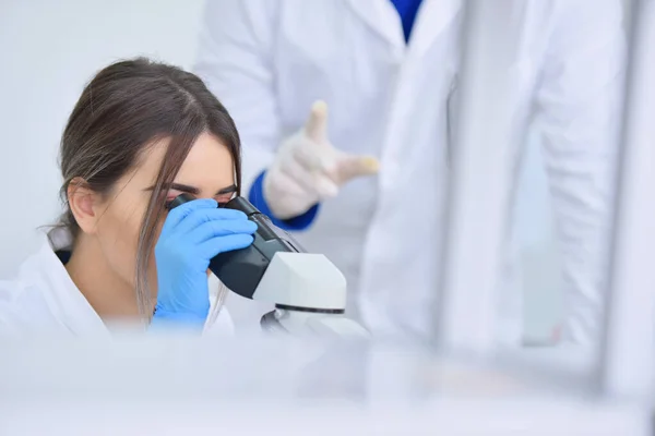Jovem cientista do sexo feminino olhando através de um microscópio em um la — Fotografia de Stock