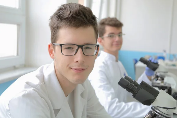 Två unga manliga forskare tittar genom ett mikroskop i ett labo — Stockfoto