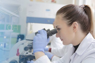 Genç bayan bilim adamı mikroskopla bir çalışmanın içine bakıyor.