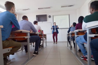 Erkek profesör öğrencilere ders veriyor ve onlarla iletişim kuruyor.