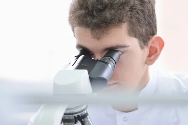 Joven científico masculino mirando a través de un microscopio en un laboratorio — Foto de Stock