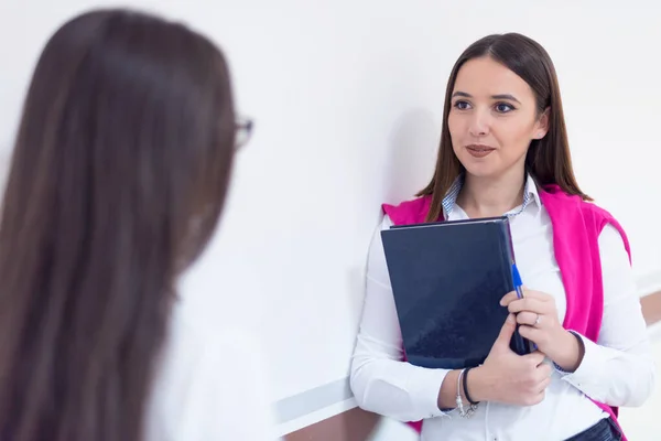 Zwei junge Studentinnen stehen mit Büchern und Taschen auf dem Flur der Universität — Stockfoto