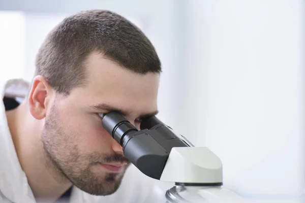 Молодой ученый-мужчина смотрит в микроскоп в лаборатории — стоковое фото