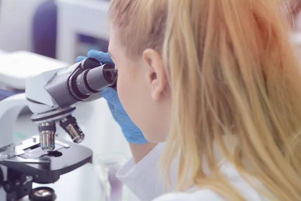 Joven científica masculina mirando a través de un microscopio en a la — Foto de Stock