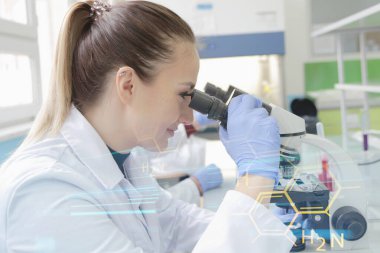 Genç bayan bilim adamı mikroskopla bir çalışmanın içine bakıyor.