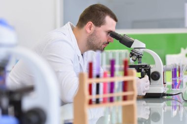 Genç bilim adamı bir laboratuarda mikroskoptan bakıyor.