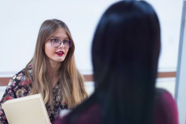 Koridorda kitap ve çantalarla duran iki genç kız öğrenci.