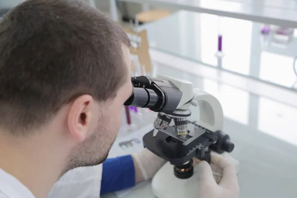 Cientista masculino novo que olha através de um microscópio em um labo — Fotografia de Stock