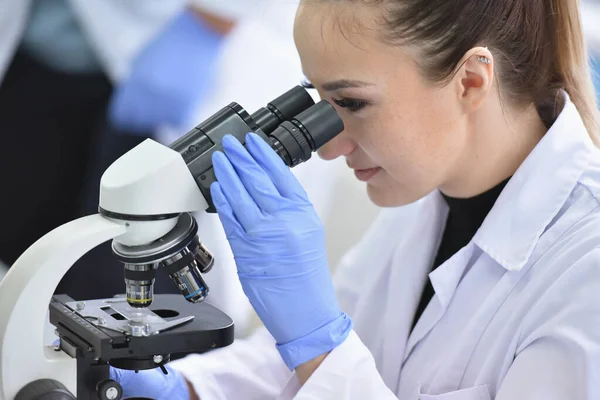 Jeune scientifique femelle regardant à travers un microscope dans une la — Photo