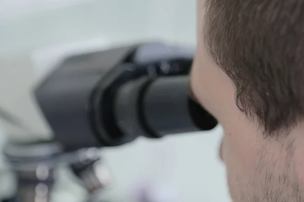 Cientista masculino novo que olha através de um microscópio em um labo — Fotografia de Stock