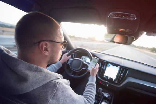 Hombre mirando el teléfono móvil mientras conduce un coche . — Foto de Stock