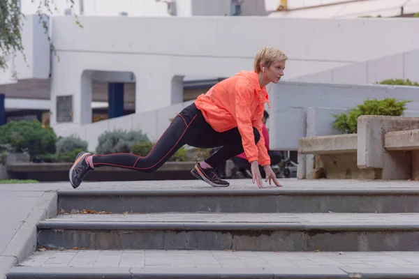 Ung kvindelig løber forbereder sig på jogging i byens gade. F - Stock-foto