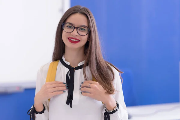 Cute female student wearing glasses with long brown holding a book bag on her back in the classroom.