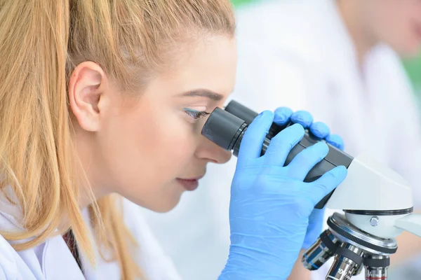 Jeune femme scientifique regardant à travers un microscope dans un laboratoire — Photo