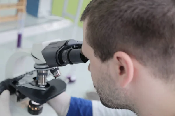 Cientista masculino novo que olha através de um microscópio em um labo — Fotografia de Stock