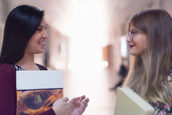 Twee jonge vrouwelijke studenten met boeken en tassen in de gang Universiteit — Stockfoto