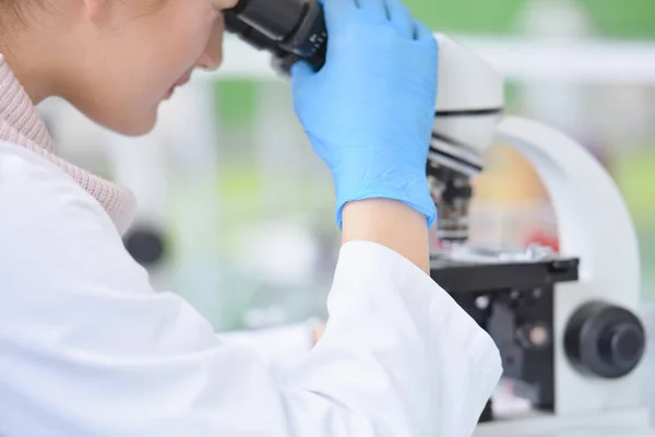 Jeune scientifique femelle regardant à travers un microscope dans une la — Photo