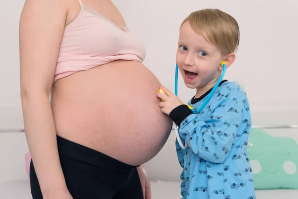 Escuchando el tummy. Curioso chico de ojos oscuros que se siente muy bien. — Foto de Stock