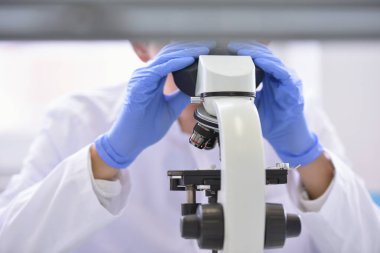 Genç bilim adamı bir laboratuarda mikroskoptan bakıyor.