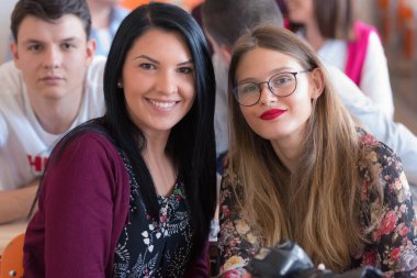 Sınıfta mutlu üniversite öğrencileri gülümseyerek kameraya bakıyor.