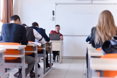 Erkek profesör öğrencilere ders veriyor ve onlarla iletişim kuruyor.
