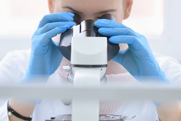 Young female male scientist looking through a microscope in a la