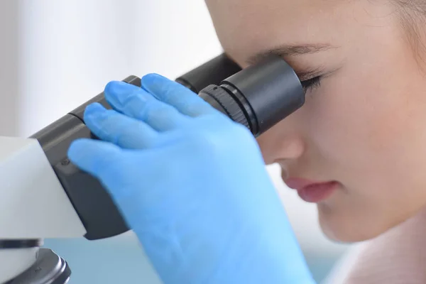 Jeune scientifique femelle regardant à travers un microscope dans une la — Photo