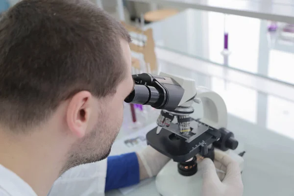 Young male male scientist looking through a microscope in a labo — Stock Photo, Image