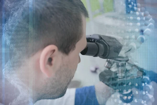 Young male male scientist looking through a microscope in a labo — Stock Photo, Image