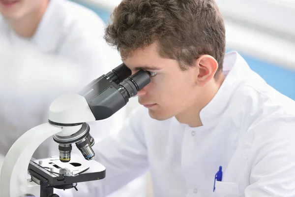 Jeune homme scientifique regardant à travers un microscope dans un laboratoire — Photo